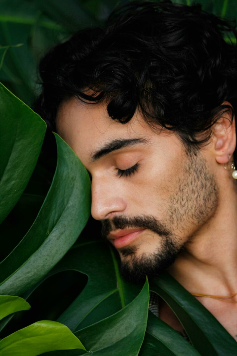 Close-up portrait of a man embracing green leaves, exuding tranquility and nature connection.