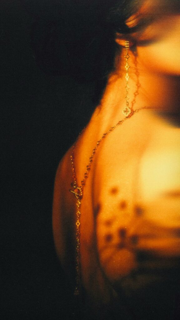Soft-focus portrait of a woman with elegant jewelry under warm, moody lighting.