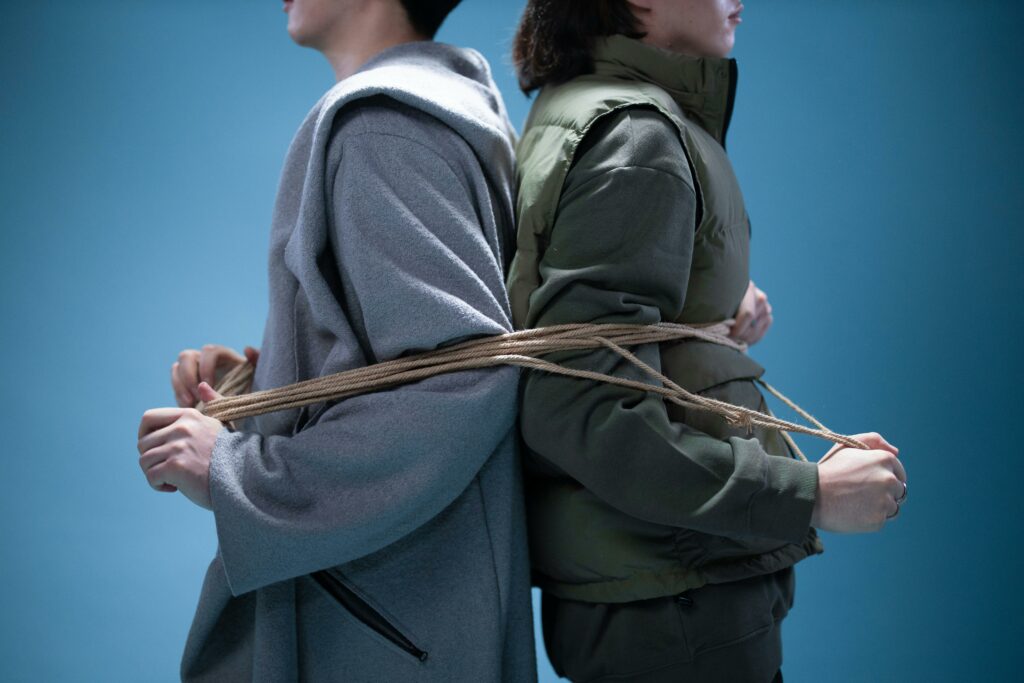 Two people tied back to back with rope on a blue background, representing connection or constraint.