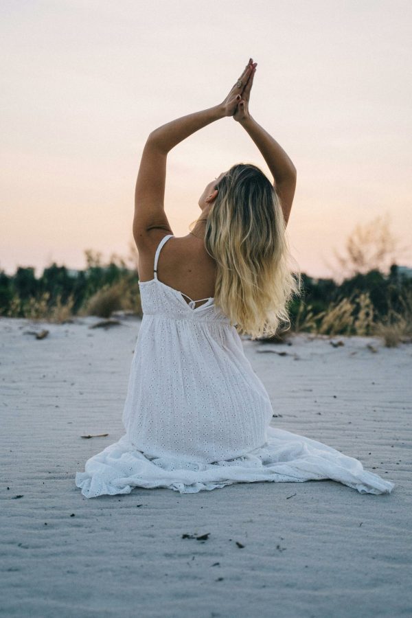Woman in a white dress meditating on a serene beach during sunset, enhancing calmness and mindfulness.
