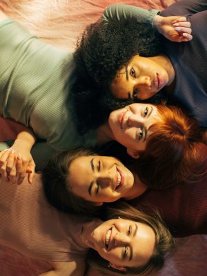 Portrait of four diverse women lying down together smiling warmly at the camera.