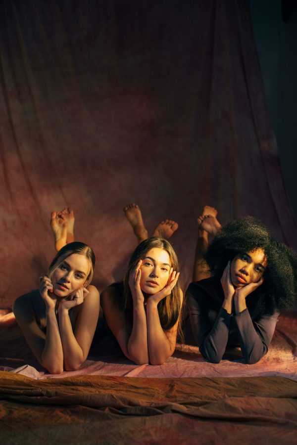 Three diverse women pose together on the floor in a studio, conveying empowerment and unity.